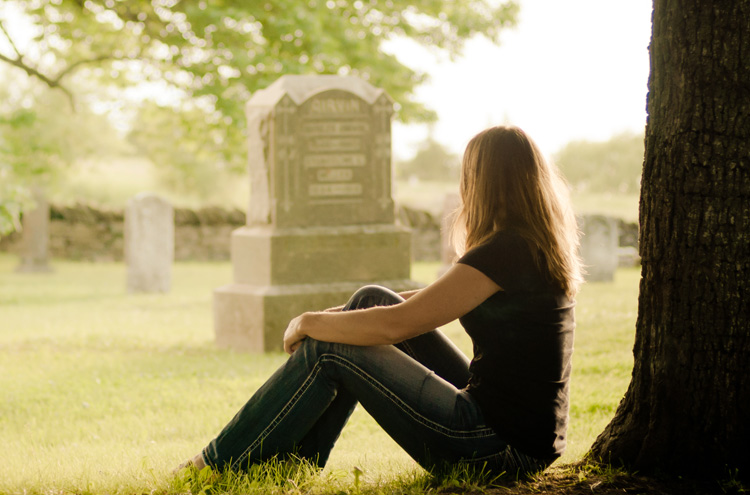 Woman sitting against tree, looking at a graveyard - What happens when you die?