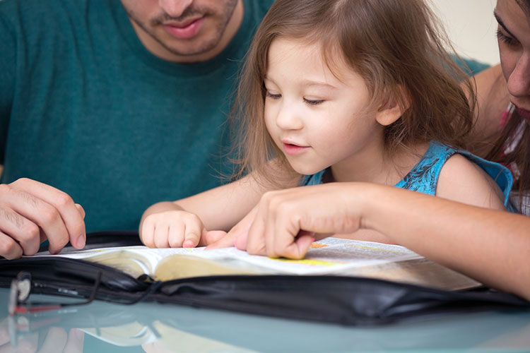 Picture of little child reading Bible with her parents